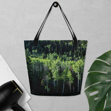 Load image into Gallery viewer, Tote bag full print with a pando forest landscape, hanging on the wall. Comparing size with hair dryer and an leave of plant