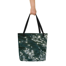 Load image into Gallery viewer, A beautiful tote bag with a brilliant reflection in the turquoise water. Black handle and carried in hand to show size.