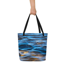 Load image into Gallery viewer, A fully printed tote bag, blue crystal clear water and rocks at the bottom, black beams, carried by one hand. Front side
