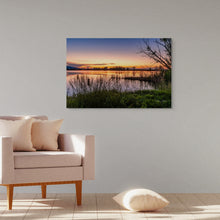 Load image into Gallery viewer, A photograph 24x36" of the sunset at Bountiful Lake and a blue heron among the branches, a mix of orange, pink and green colors displayed in a living room
