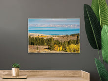 Load image into Gallery viewer, "'Enchanting Hues' 16" x 24" - Gracing a greyish wall, complemented by wooden furniture and a potted plant, creating a serene and sophisticated ambiance."