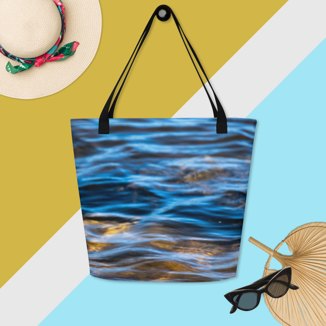 A fully printed tote bag, crystalline water and rocks in the background, black beams, hung and accompanied with everyday accessories to show the size