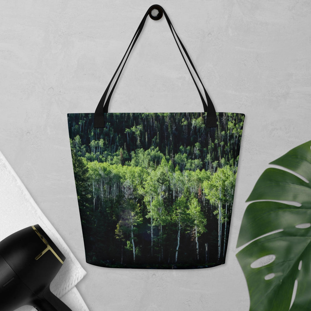 Tote bag full print with a pando forest landscape, hanging on the wall. Comparing size with hair dryer and an leave of plant