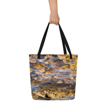 Load image into Gallery viewer, A fully printed tote bag, crystal clear water and rocks at the bottom, black beams, carried by one hand. The other side of the bag
