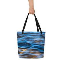 Load image into Gallery viewer, A fully printed tote bag, blue crystal clear water and rocks at the bottom, black beams, carried by one hand. Front side
