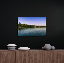 Load image into Gallery viewer, A pic title Beginnin of Autumn in Hyrum Reservoir hanging on black wall over brown desk, contrasting for it brilliant blue and magenta colors.
