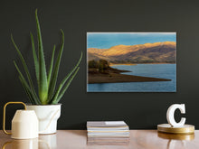 Load image into Gallery viewer, &#39;Sunset Over The Mountains&#39; - 16&quot;x24&quot; on a black wall in a small corporate setting, displayed on a wooden table with magazines and a potted cactus for size reference.
